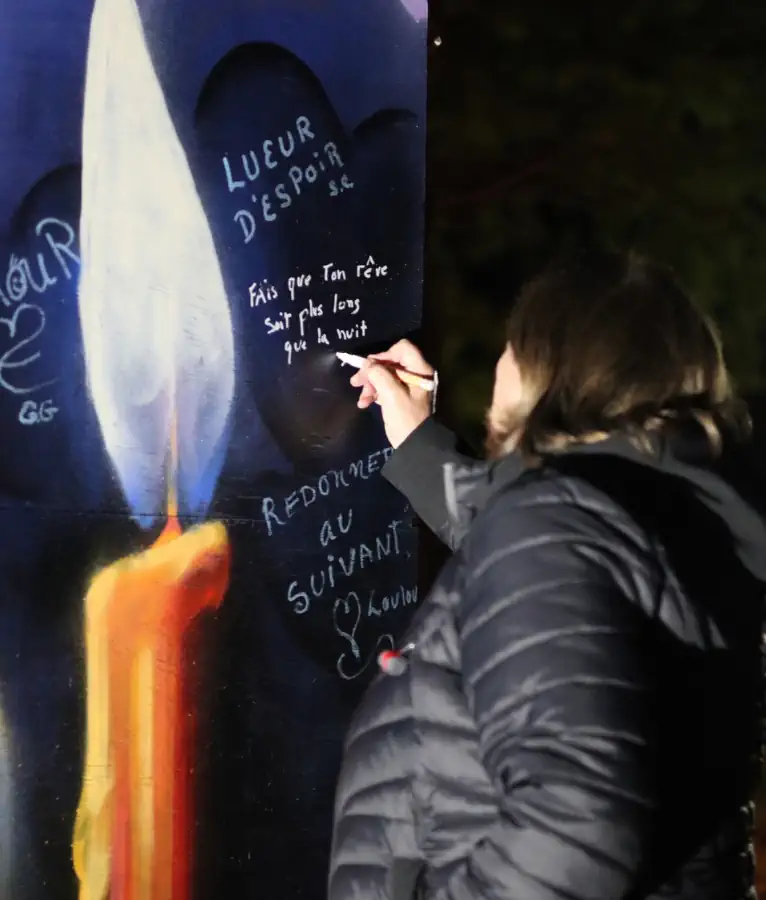Une femme écrit un message sur une murale faite en sensibilisation à l'itinérance à l'occasion de la Nuit des sans-abris 2026 à Bécancour.